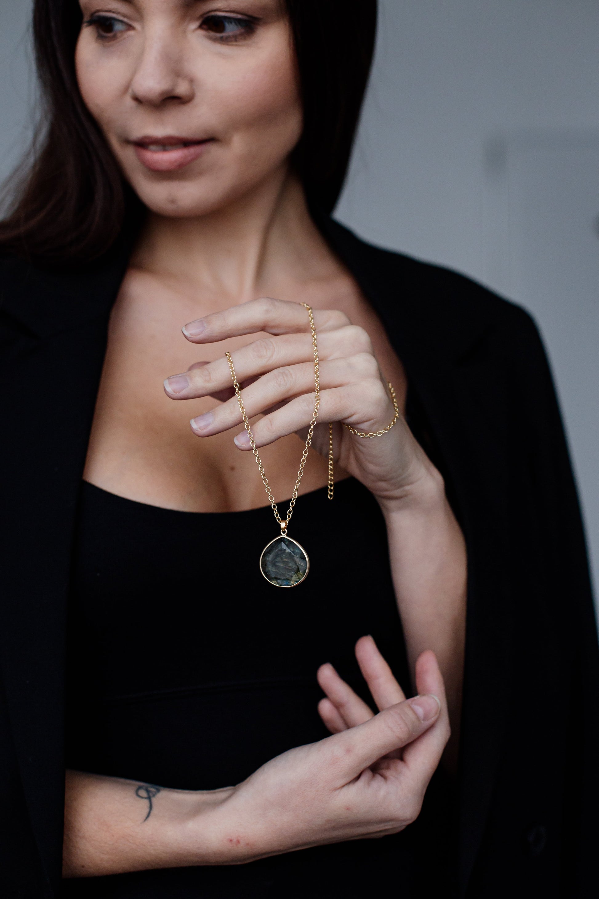 Frau mit schwarzem Blazer hält goldene Halskette mit rundem Anhänger.