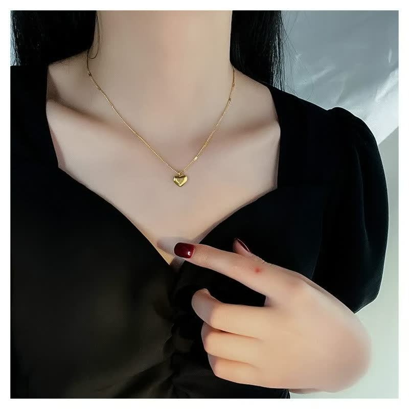Frau mit goldener Herz-Halskette, schwarzes Kleid, elegante Modeaccessoires.