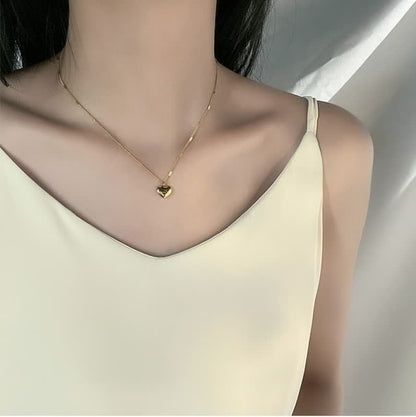Frau mit goldener Herz-Halskette, elegantes Design, modisches Accessoire, minimalistisch.