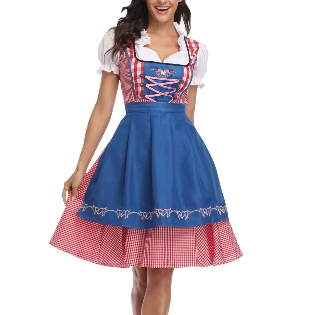 Model i dirndl med klarblåt forklæde over rød-hvidt ternet skørt, pink snøring i livet og hvide pufærmer, set forfra. 3