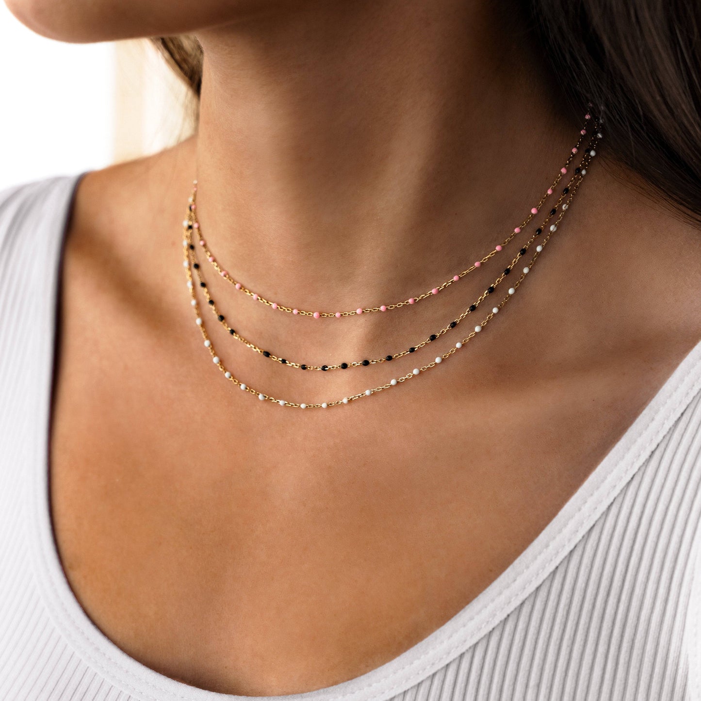 Frau trägt mehrlagige Halskette aus Gold mit schwarzen und rosa Perlen, eleganter Schmuck.