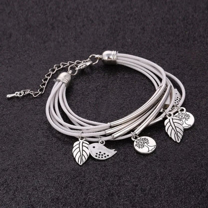 Mehrlagiges Armband aus Leder mit silbernen Baum- und Blattanhängern auf schwarzem Hintergrund.