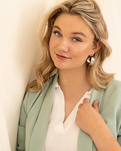 Frau mit silbernen Chunky Hoops Ohrringen, mintgrüner Blazer, weißes Hemd.